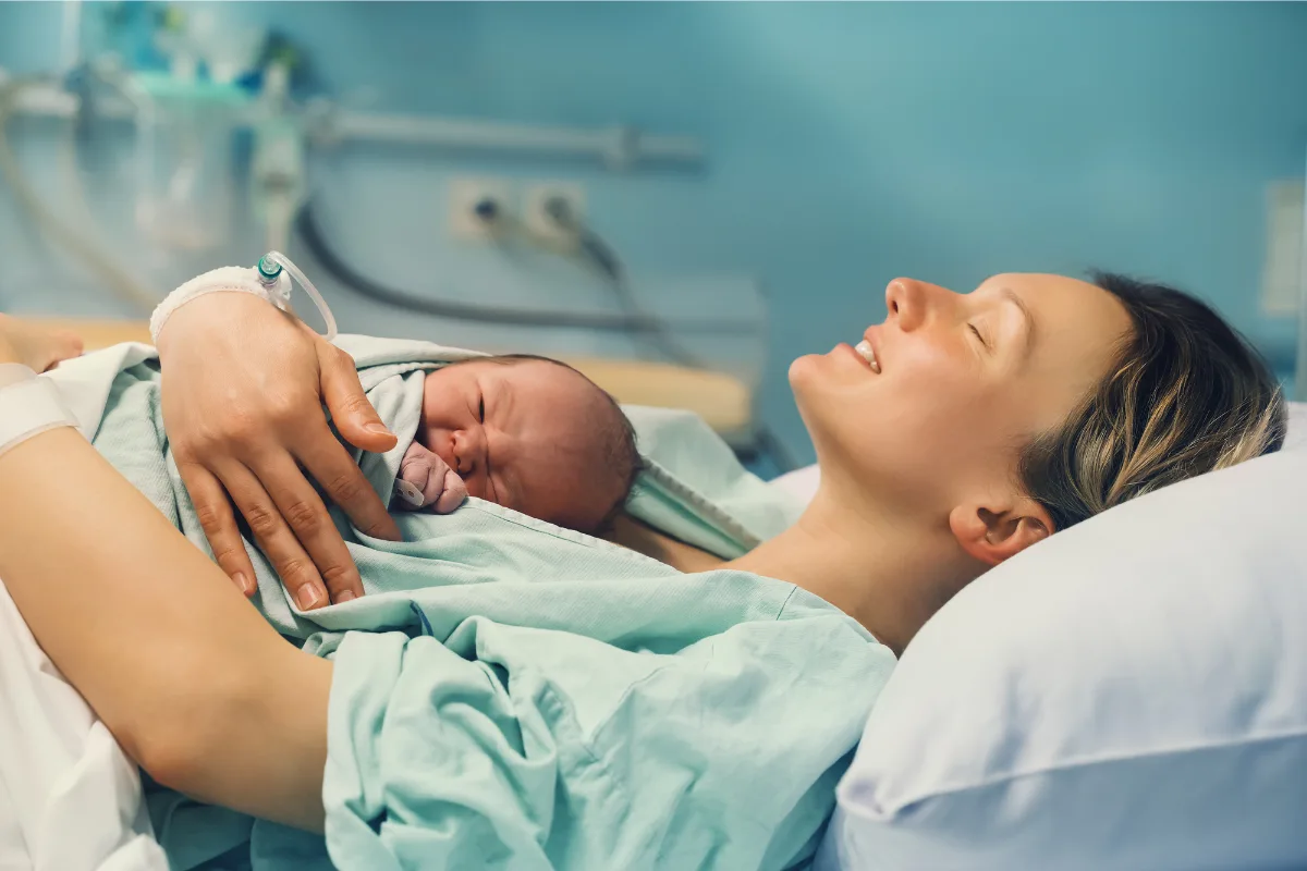 New mother smiling and holding newborn baby after pregnancy care in Edmonton
